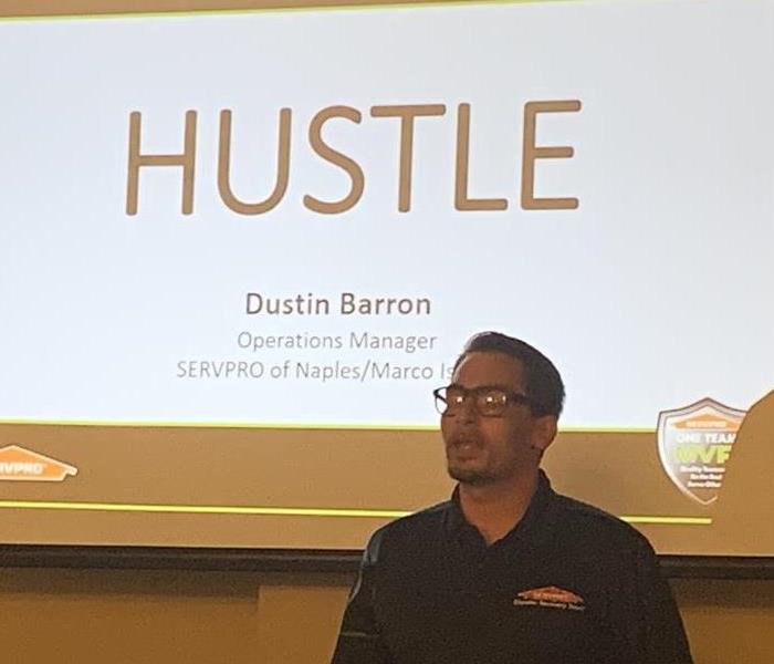SERVPRO employee standing in front of a projection screen with the word Hustle on it. 