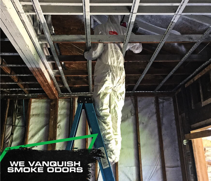 SERVPRO tech wearing a protective gear while inspecting fire damage in a home with the caption: WE VANQUISH SMOKE ODORS